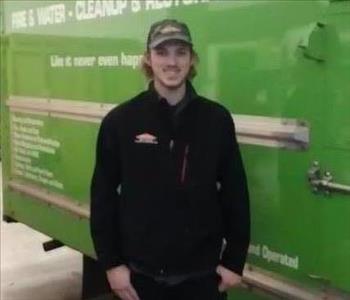 Male employee standing in front of a green SERVPRO vehicle
